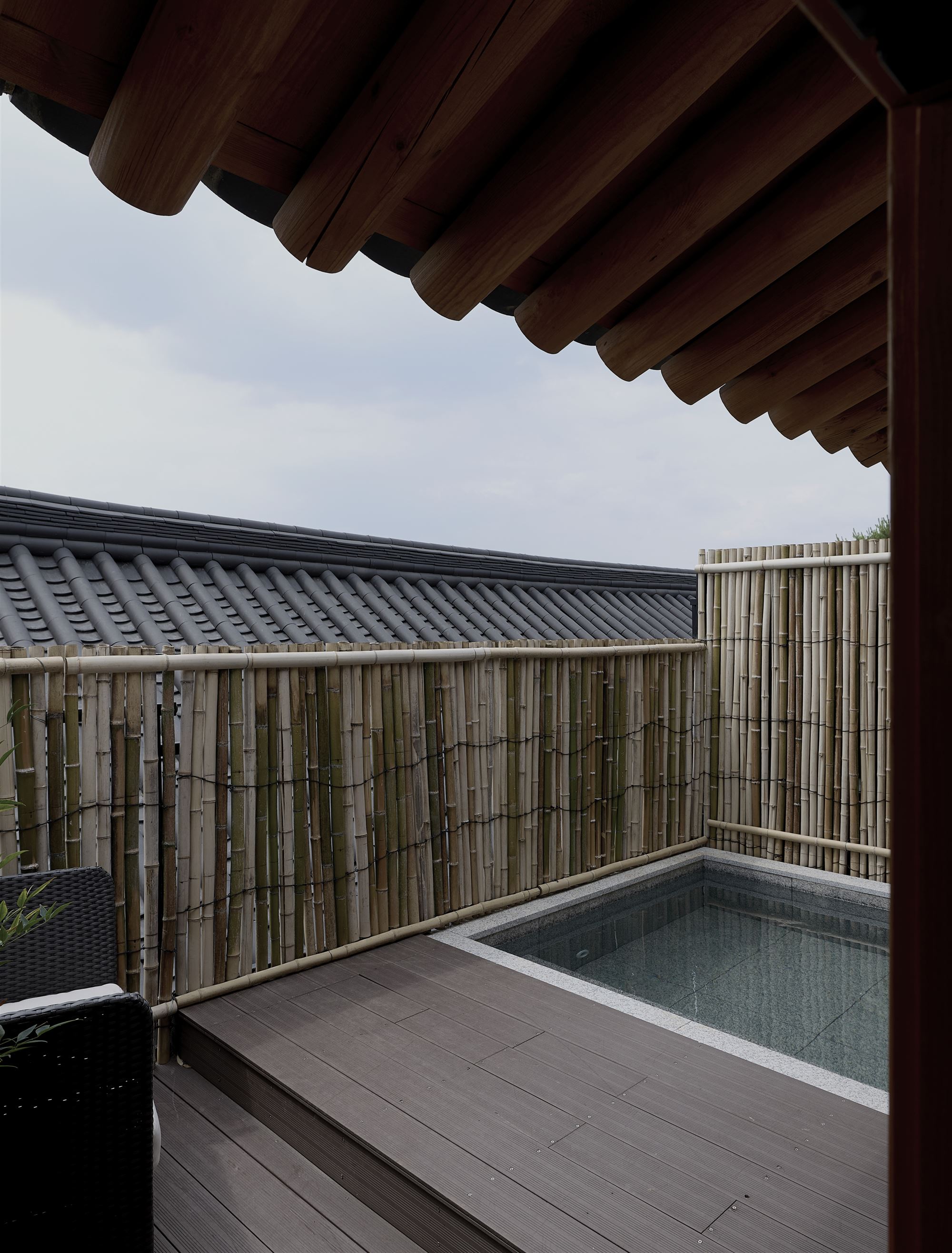 An outdoor spa enclosed by a bamboo fence beneath the eaves