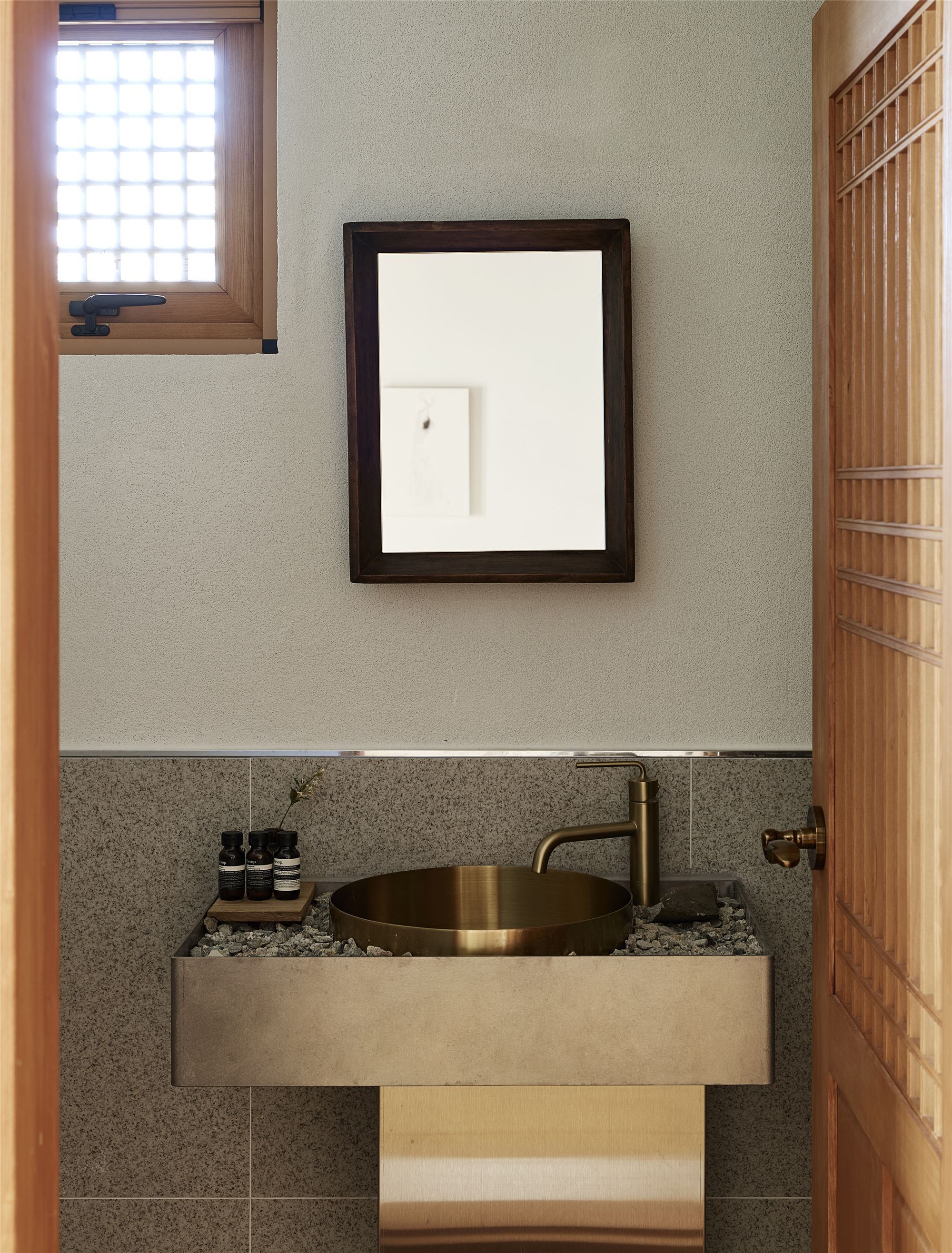 A bathroom with a small side window and a brass sink